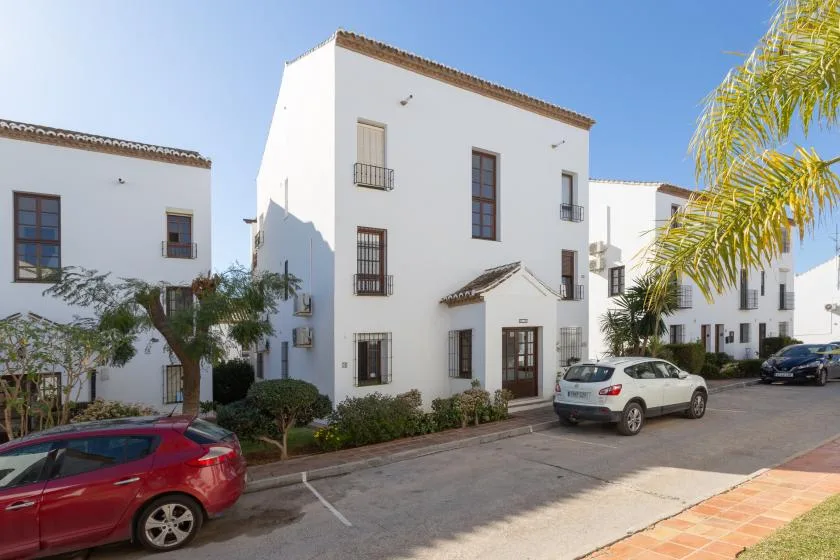 White multi-story buildings line a sunny street with parked cars and palm trees.