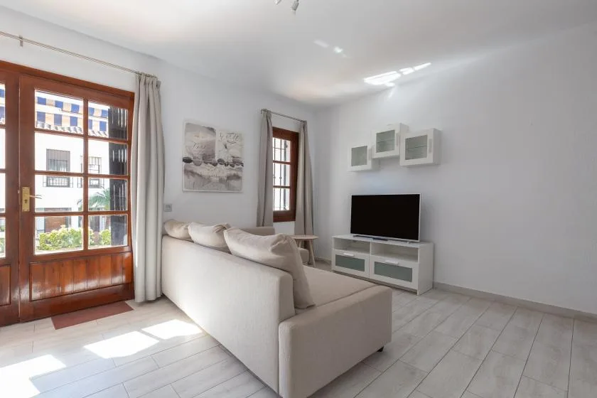 A bright living room with light seating and a television by the wall.