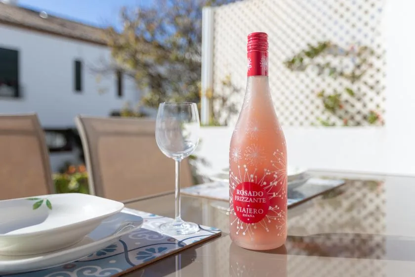 A patio dining table with a pink bottle, wineglass, and place setting.