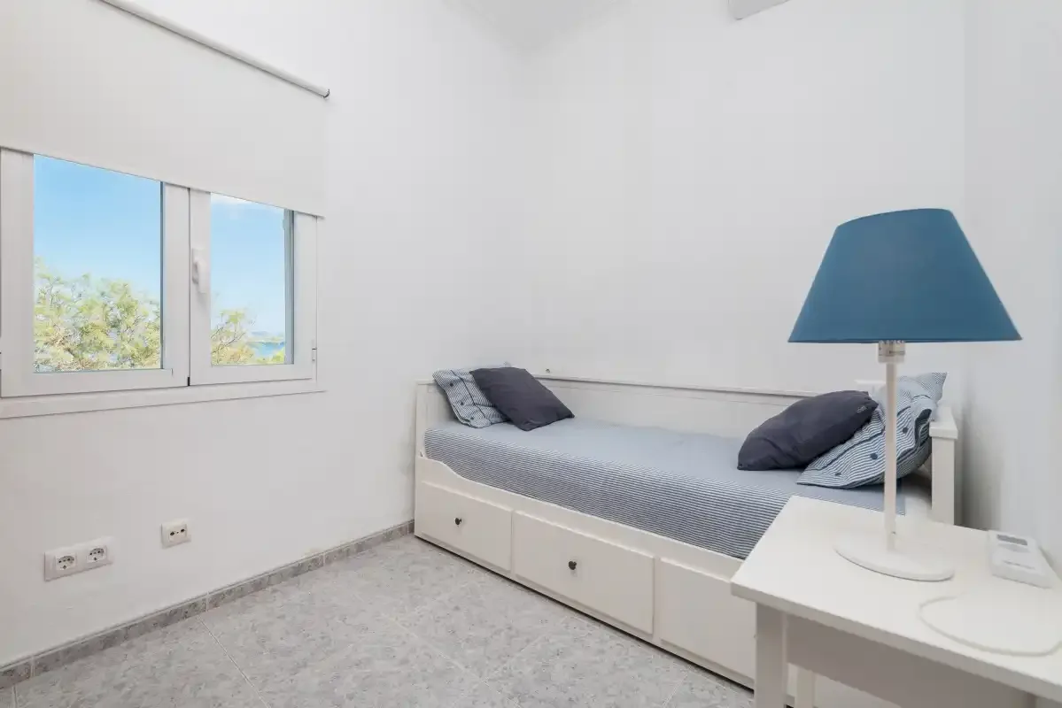 A bright bedroom with a single bed beneath a window.