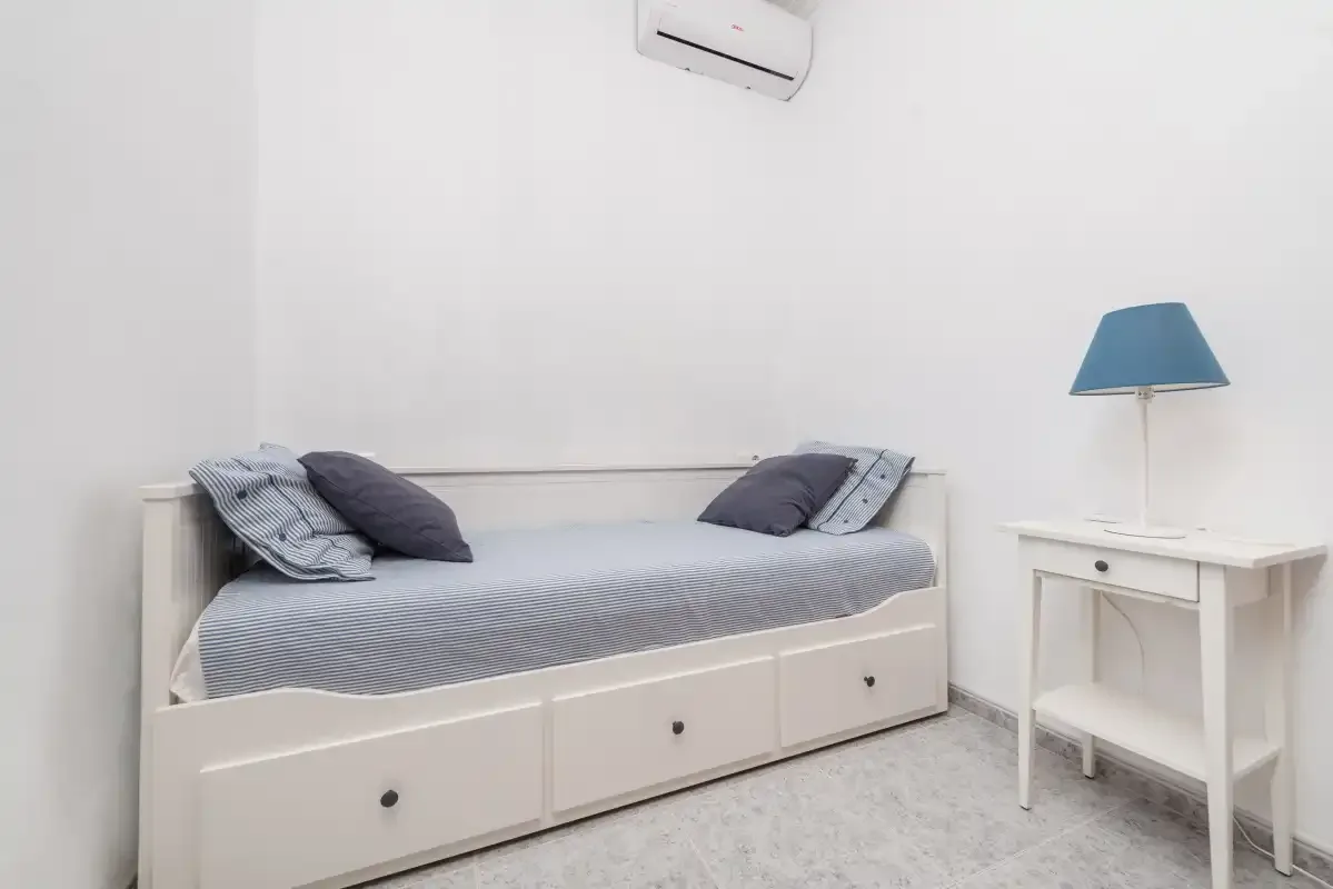 A bedroom with a single bed, pillows, and a bedside table.