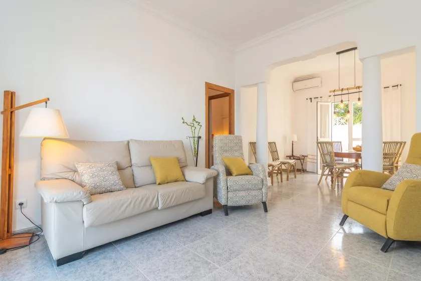 A bright living room with a sofa and armchairs opens onto a dining area.