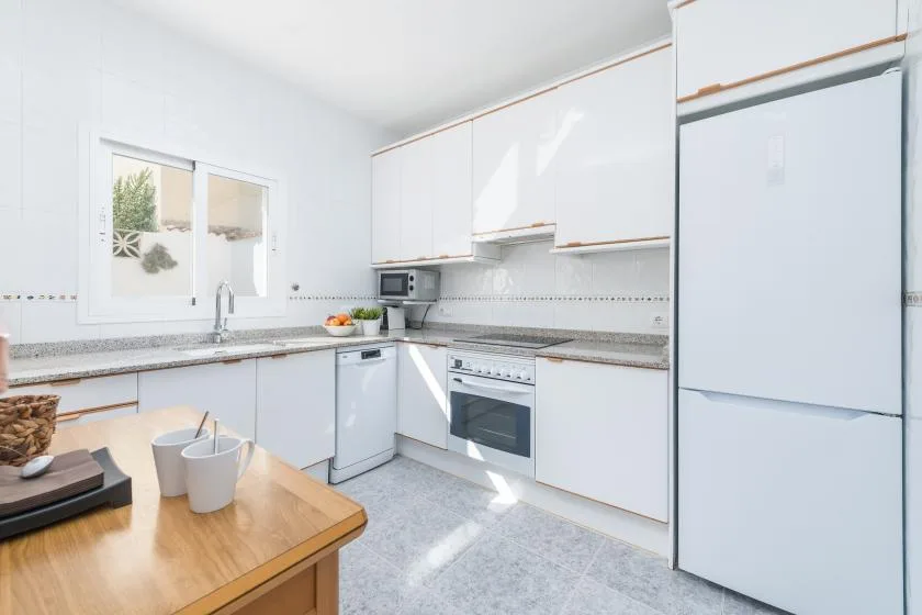 A bright kitchen with white cabinets, a refrigerator, and a countertop.