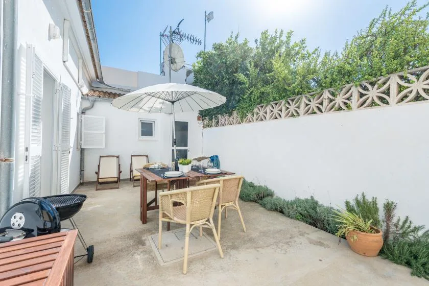 A sunny outdoor patio with a dining table, chairs, and a large umbrella.