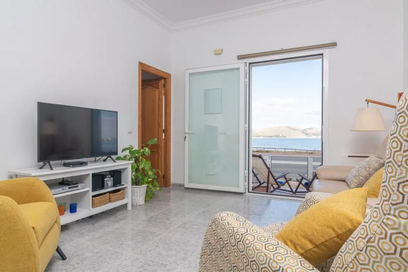 A bright living room with patterned seating and a television beside a balcony.