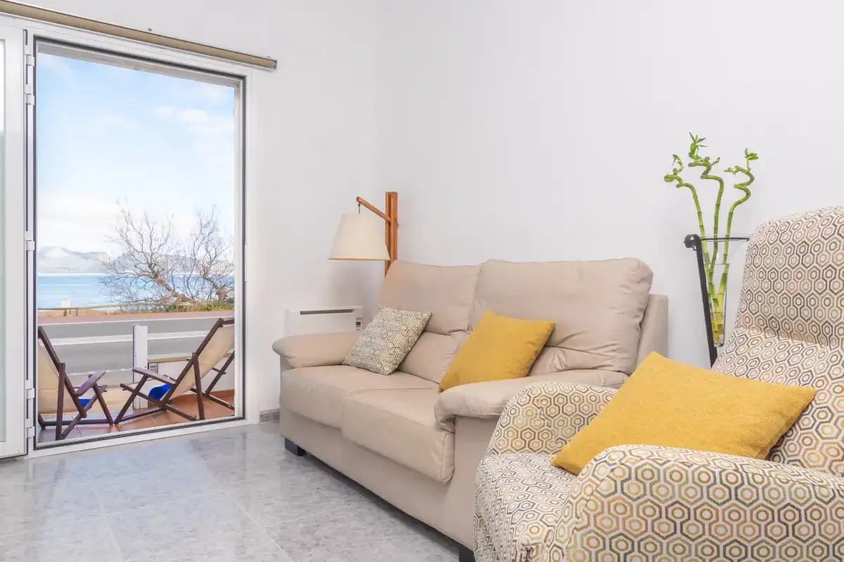 A bright living room with a beige sofa and a large window overlooking the sea.