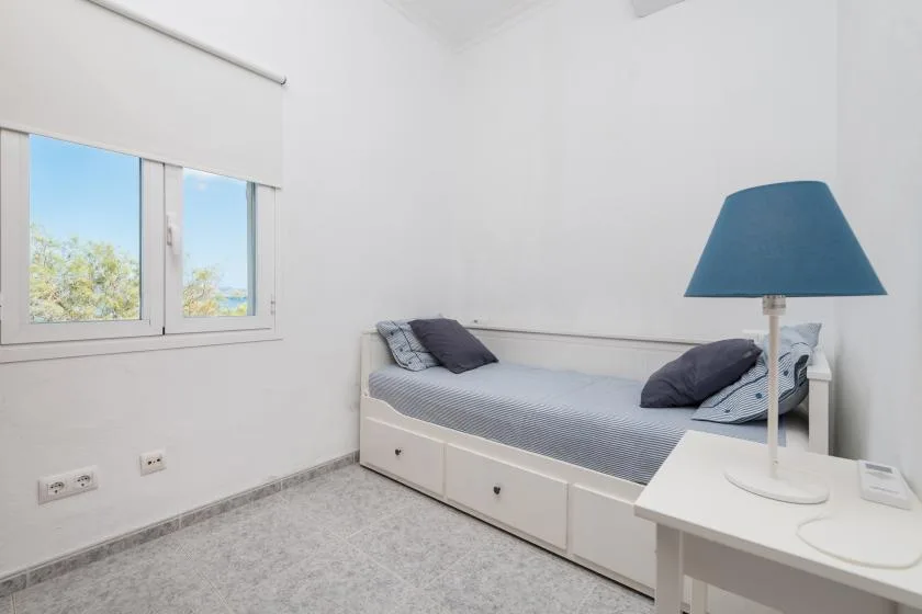 A bright bedroom with a single bed, window, and blue-shaded lamp.