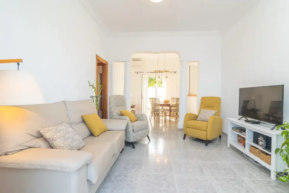 A bright living room with seating, a television, and a dining area beyond.
