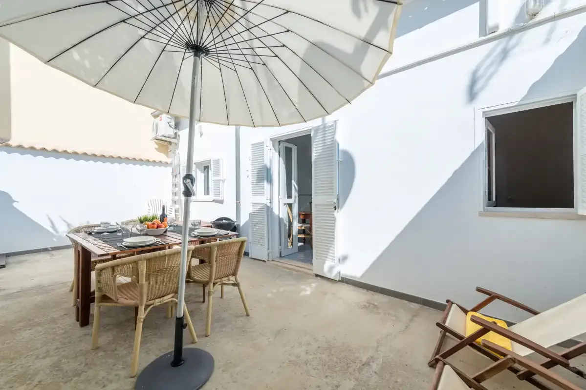An outdoor dining area with a table and chairs beneath a large umbrella.