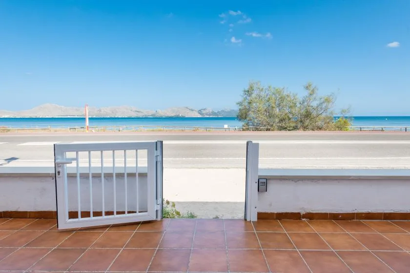 A tiled terrace overlooks a beach and the sea through an open gate.