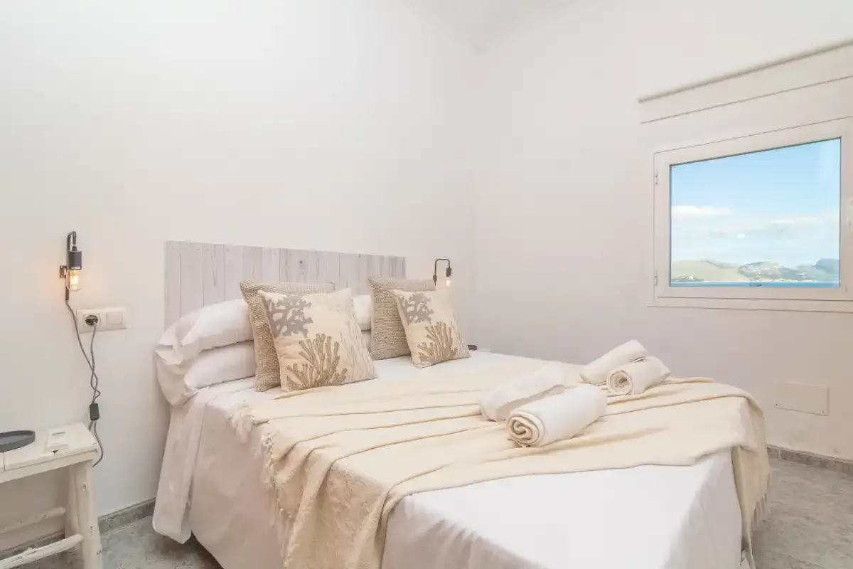 A bedroom with a neatly made bed and a window overlooking the landscape.