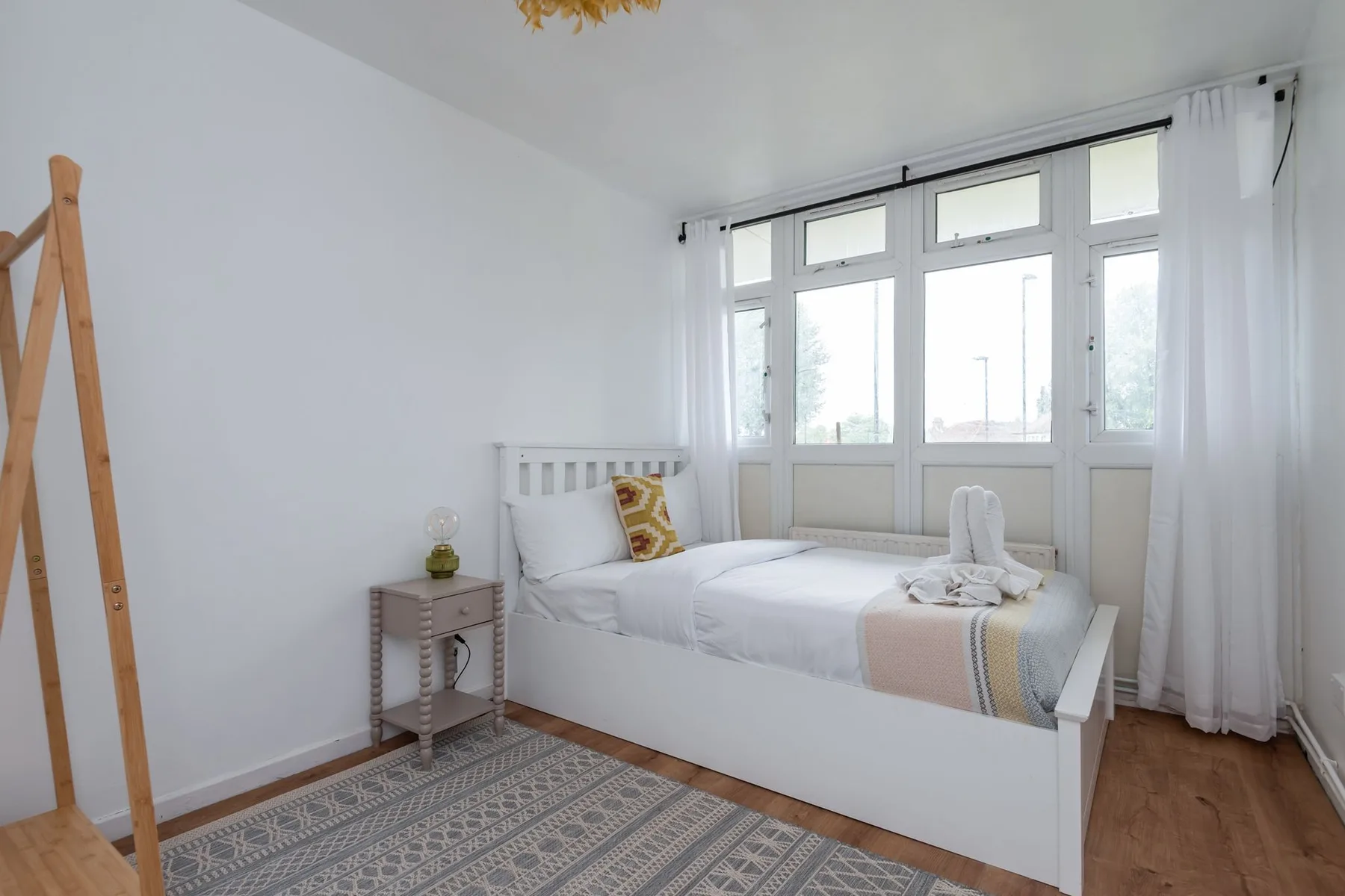 A bright bedroom with a white bed beside large windows.