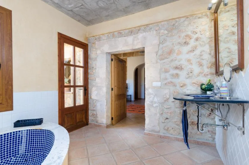 A tiled bathroom with a curved tub, stone walls, and an open doorway.