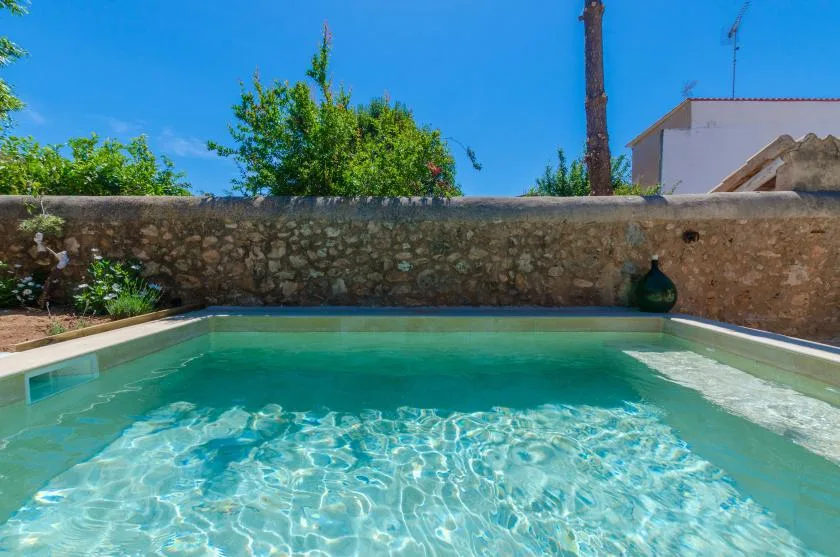 A swimming pool sits beside a stone wall beneath a clear blue sky.
