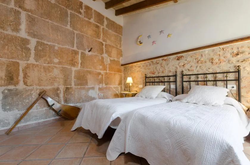 A bedroom with two beds, white bedding, and exposed stone walls.
