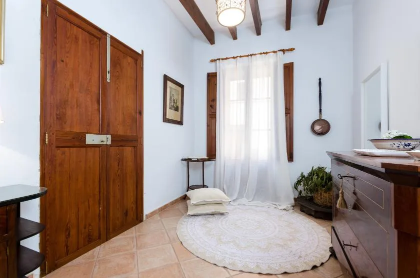 A bright room with a curtained window, wooden doors, and a round rug.