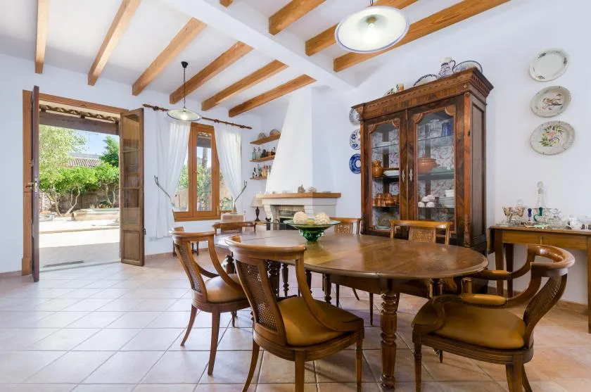 A dining room with a large wooden table and chairs beneath exposed ceiling beams.