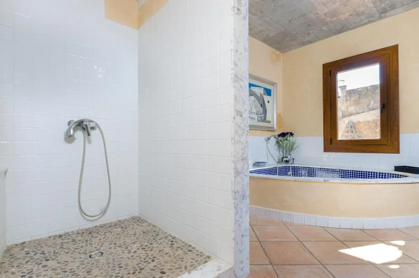 A tiled bathroom with a walk-in shower and a bathtub beneath a window.