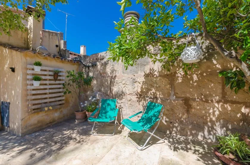 A sunny stone courtyard with turquoise lounge chairs beneath leafy trees.