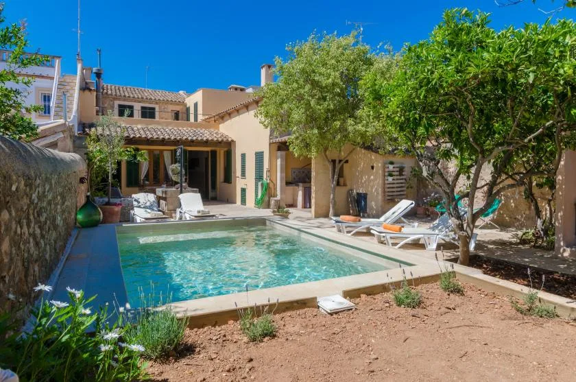 A courtyard pool beside a light-colored building, with lounge seating and trees.