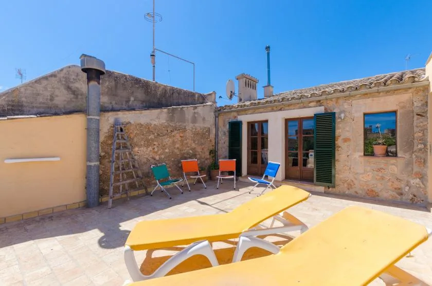 A sunny rooftop terrace with yellow loungers and seating beside a stone building.