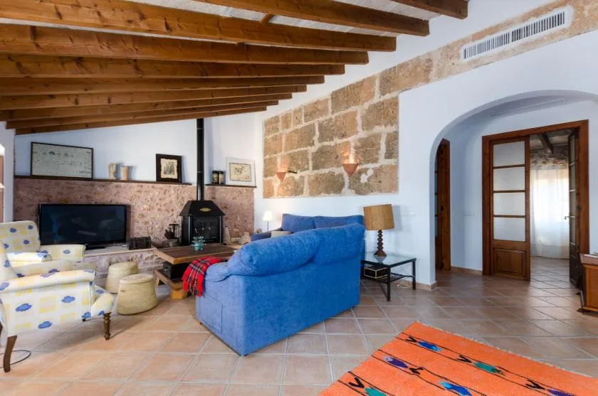 A living room with blue seating, a television, and exposed wooden ceiling beams.