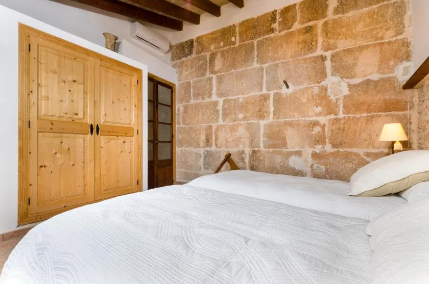 A bedroom with a white bed, wooden wardrobe, and exposed stone wall.