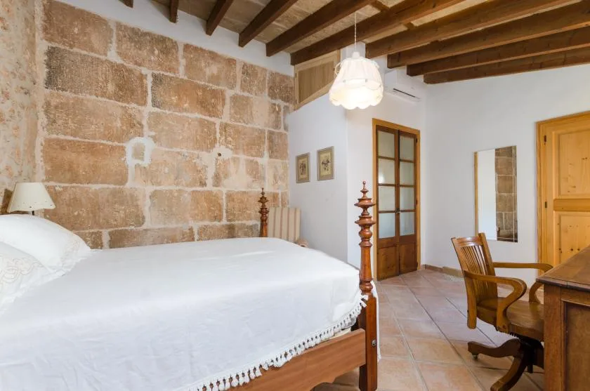A bedroom with a large bed, exposed ceiling beams, and a stone wall.