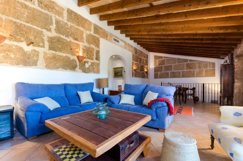 A living room with blue seating, a wooden coffee table, and exposed ceiling beams.