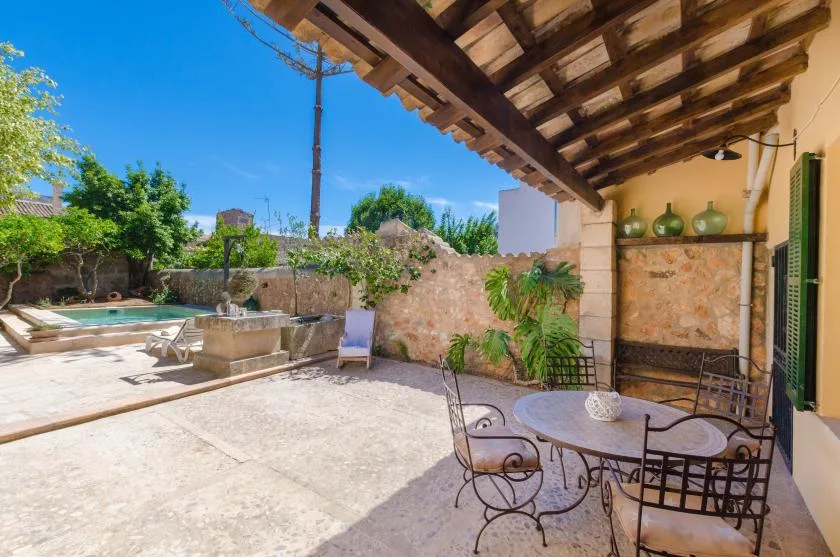 A sunny stone patio with outdoor seating, a small pool, and a wooden overhang.