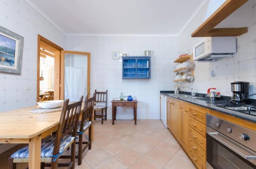 A tiled kitchen with a long dining table and wooden cabinetry.