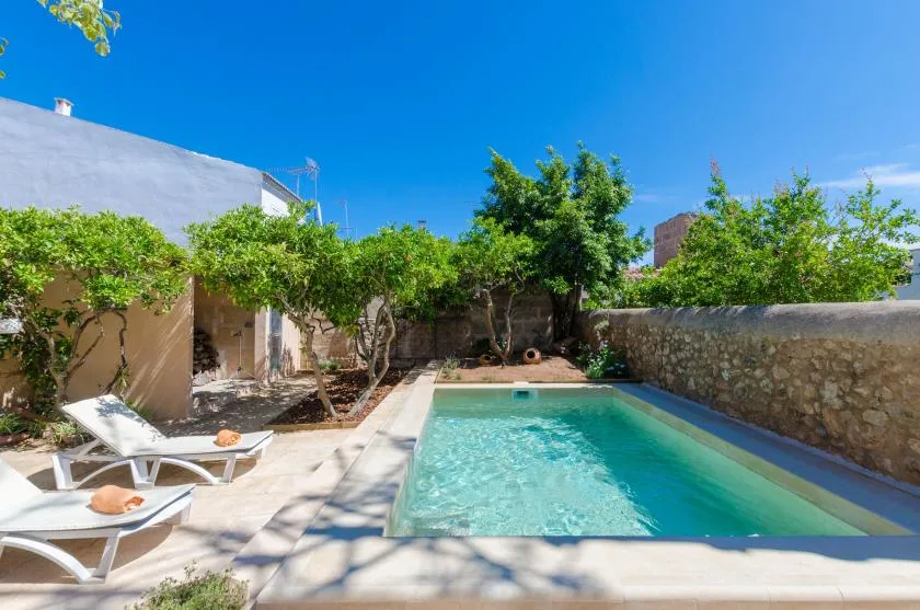 An outdoor swimming pool sits beside a stone wall and shaded seating.