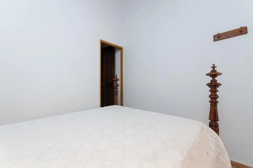 A bedroom with a large bed covered in white bedding and an open doorway.