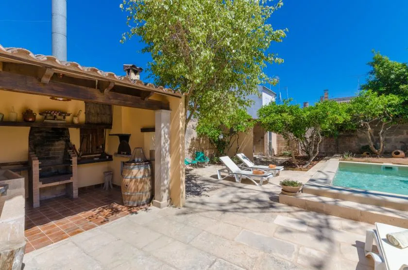 A sunny patio with a pool, lounge seating, and a covered outdoor cooking area.