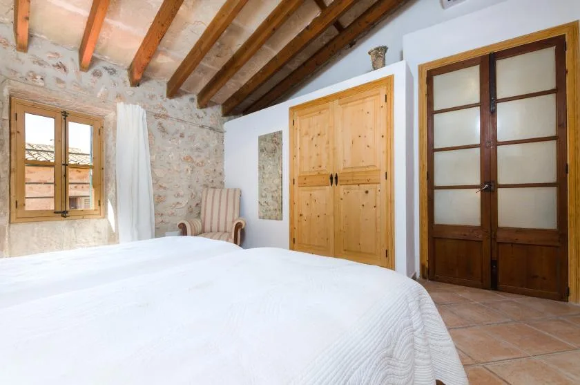 A bedroom with a large bed, exposed ceiling beams, and wooden doors.