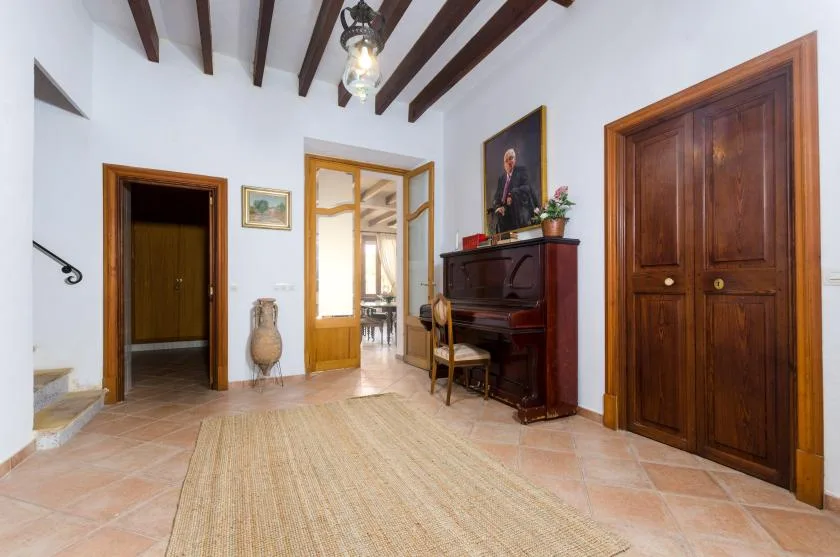 A bright tiled hallway with a piano and several wooden doorways.