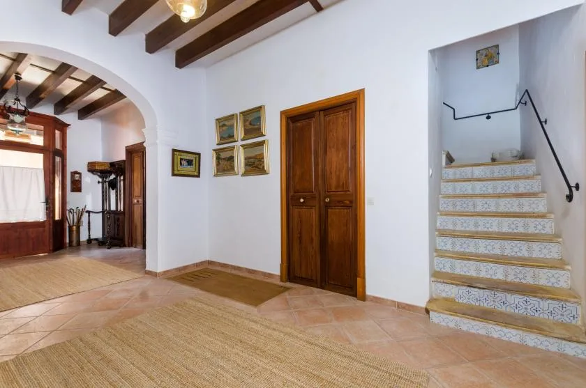 A tiled interior hallway with wooden doors, framed pictures, and a staircase.