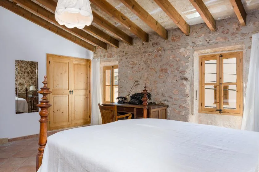 A bedroom with a white bed, wooden beams, and a stone wall.