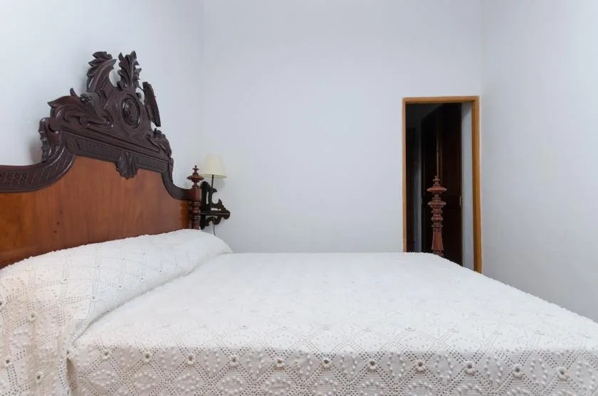 Bedroom with a bed covered by a white quilt and an ornate wooden headboard.