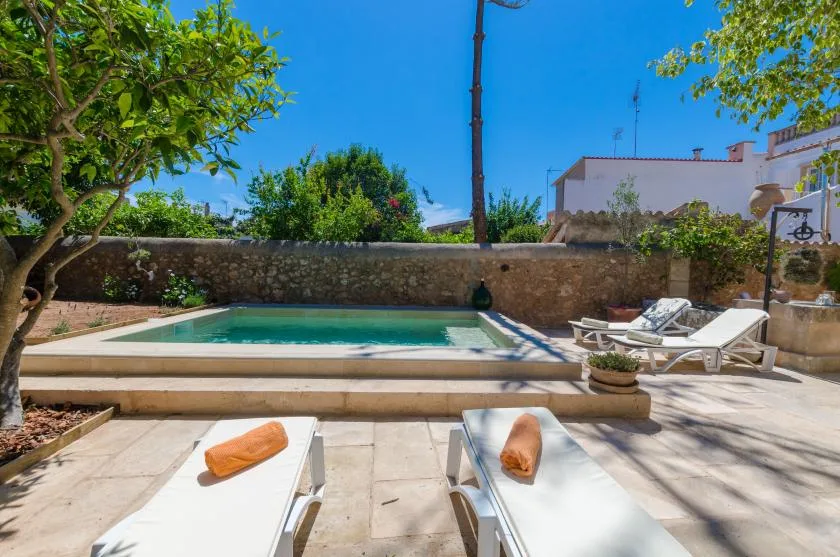 A swimming pool sits in a sunny outdoor courtyard with lounge chairs.