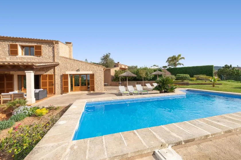 Una piscina junto a una casa de piedra, con asientos reclinables y zonas ajardinadas.