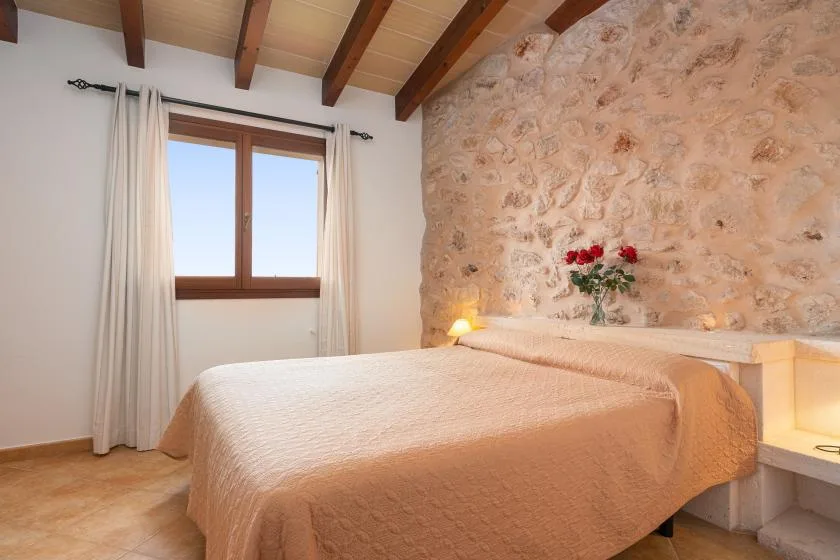 Un dormitorio con una cama junto a una pared de piedra y una ventana con cortinas.