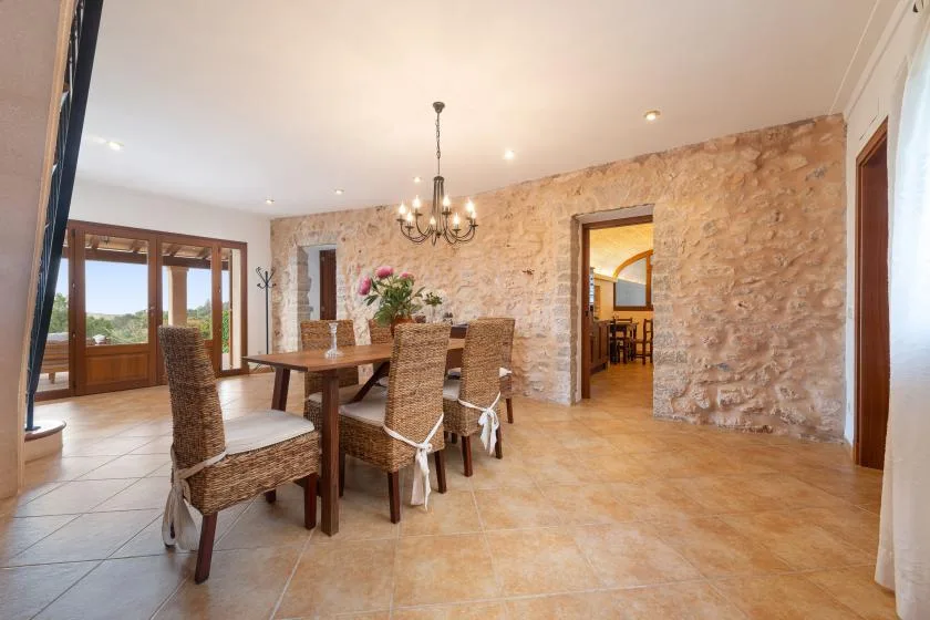 Comedor con mesa de madera y asientos de mimbre junto a una pared de piedra.
