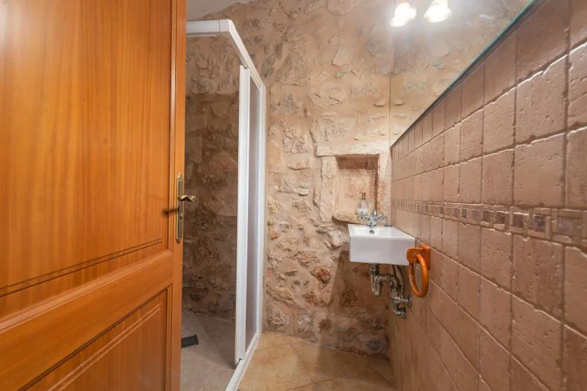 Un baño con paredes de piedra, ducha y lavabo de pared.