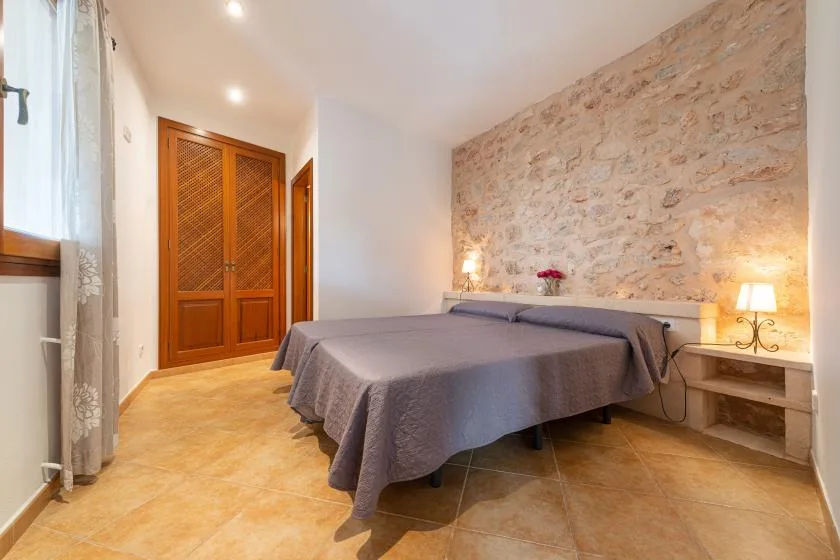 Un dormitorio con una cama junto a una pared de piedra texturizada y un armario de madera.