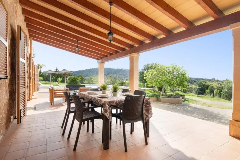 Un comedor exterior cubierto con mesa y sillas da a un paisaje verde.