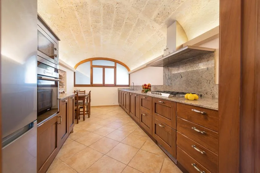 Una cocina con gabinetes de madera, suelo de baldosas y una ventana al fondo.