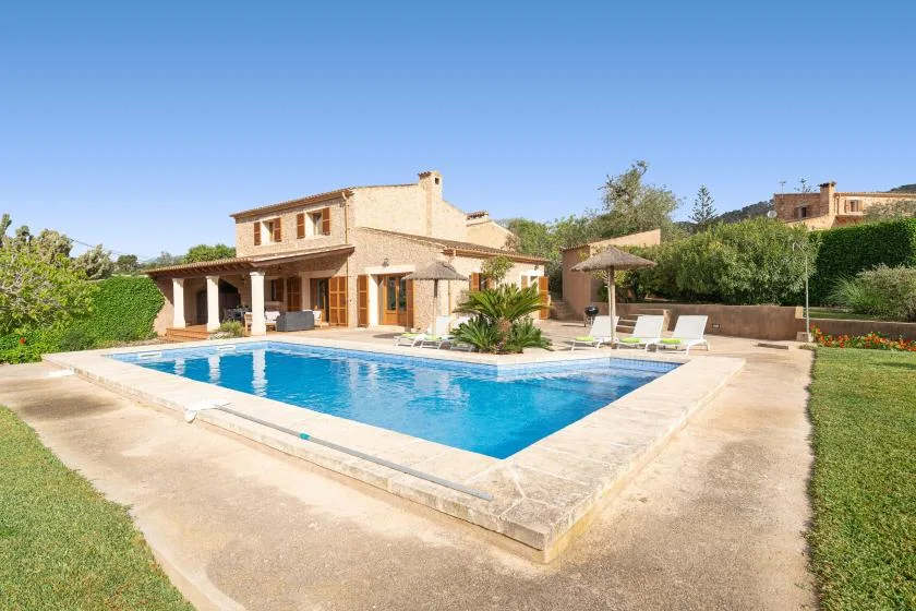 Una piscina está junto a una casa de piedra y un patio al aire libre.