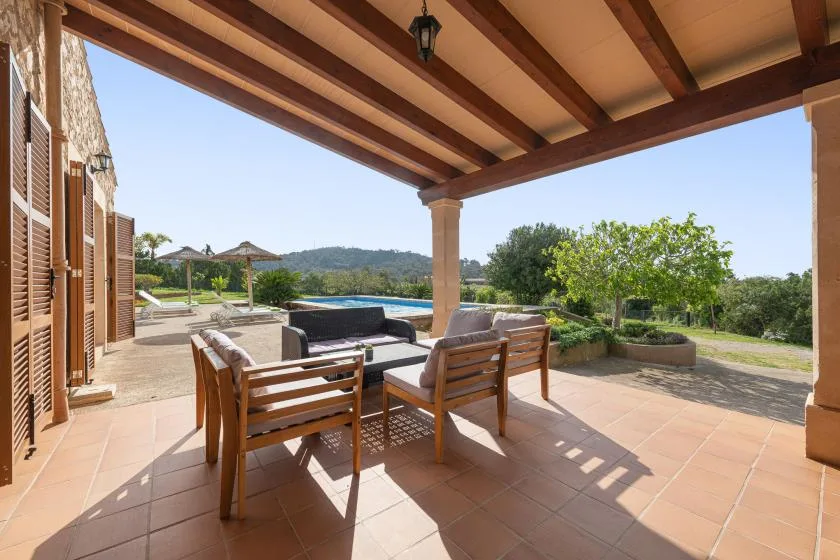 Un patio cubierto tiene asientos de madera y vistas a la piscina y al paisaje.
