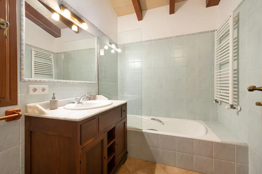 Un baño con un mueble de madera, espejo y bañera.